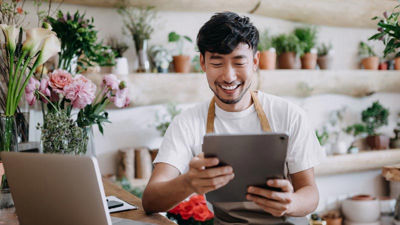 Flower shop owner smiling and looking at tablet.