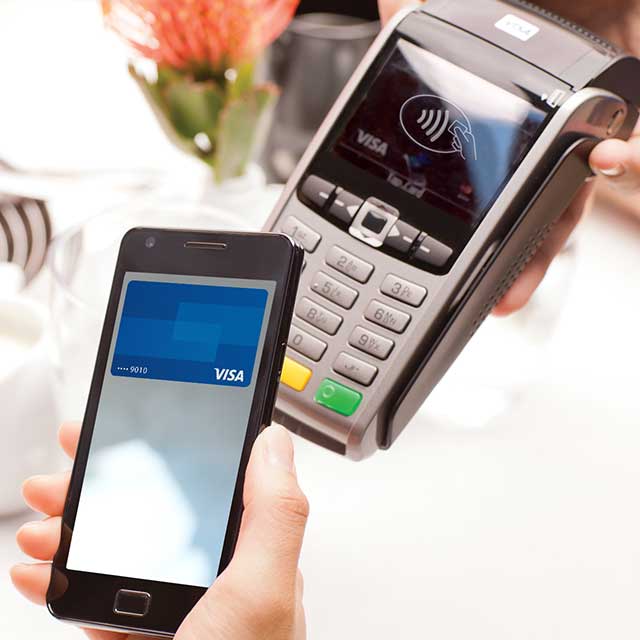 A mobile phone being held over a checkout terminal displaying the Contactless Symbol.