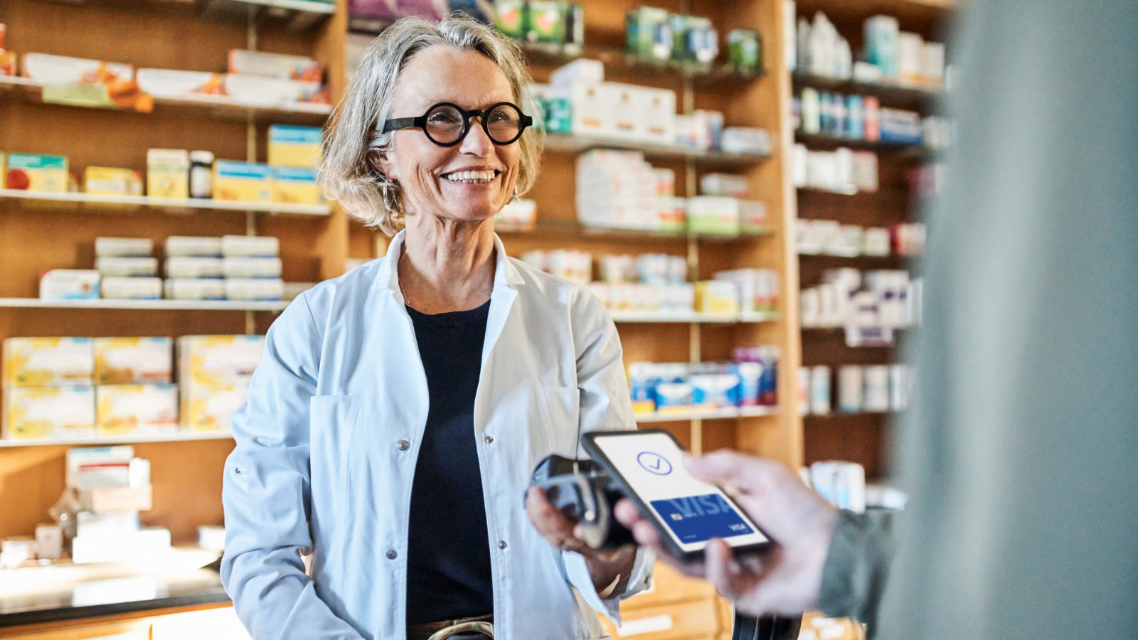 Woman behind pharmacy counter with a man paying via visa mobile