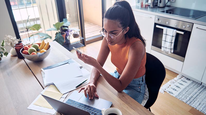 woman at desk using mobile and laptop